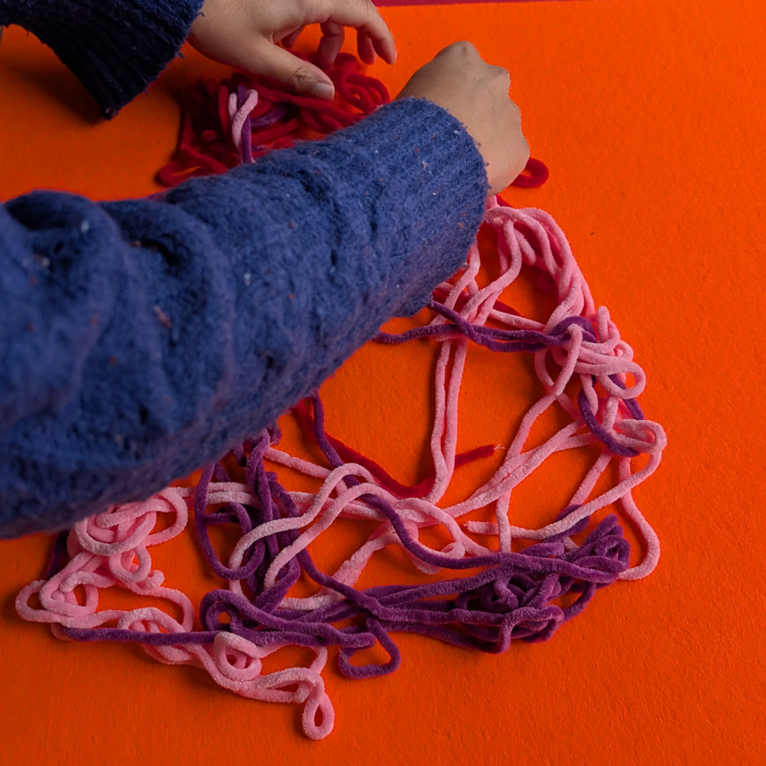 hands playing with colorful pink and red lines looking like a bowel.